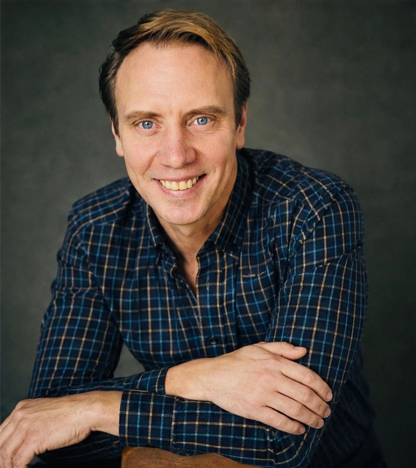 Retrato de estudio de Sergio Chernykh sonriendo, con camisa de cuadros azul